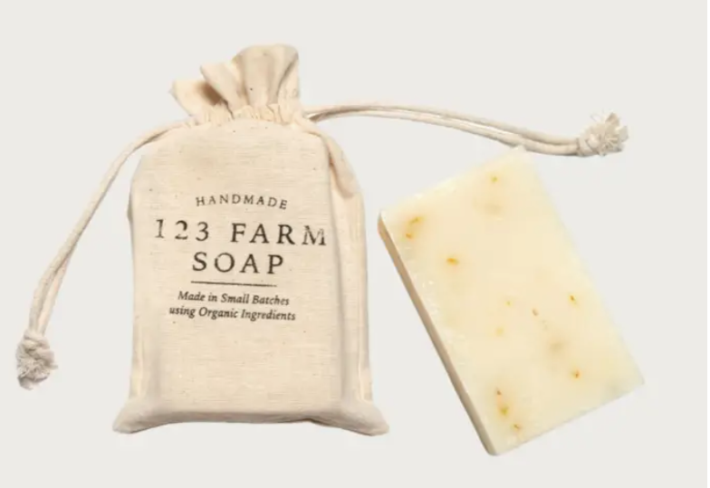 Handmade pink grapefruit soap with a drawstring bag labeled '123 Farm Soap' on a light background